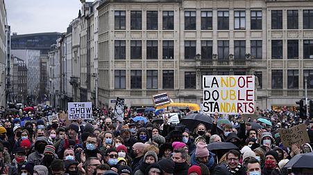 A man holds a sign which reads 'Land of double standards' as he protests with other artists during a demonstration in Brussels