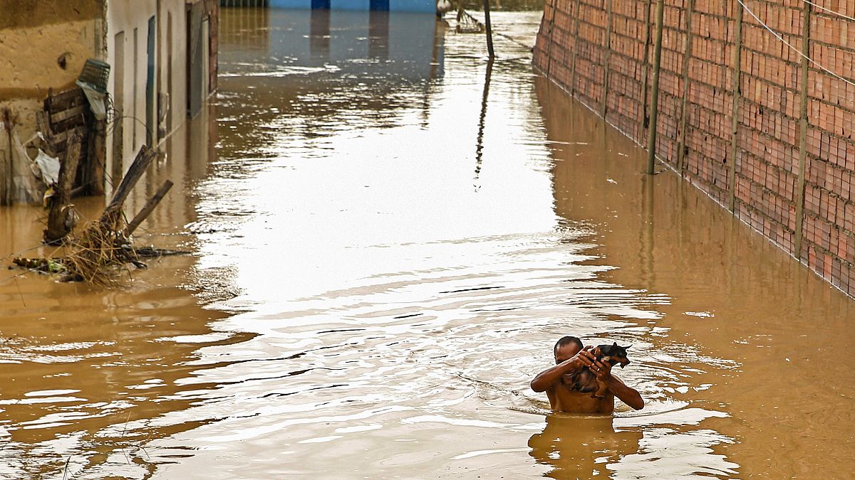 Un hombre lleva a su perro sobre las aguas de la inundación, 27/12/2021, Itapetinga, Brasil