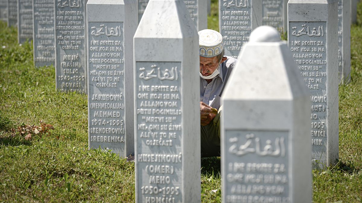 رجل يصلي جالسًا بين حجارة القبور في بوتوكاري بالقرب من سريبرينيتشا - البوسنة. 2020/07/11