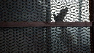 صورة أرشيفية لأحد أعضاء جماعة الإخوان المسلمين يلوح بيده من داخل قفص المتهمين في قاعة محكمة بسجن طرة، جنوب القاهرة، 22 آب/أغسطس 2015