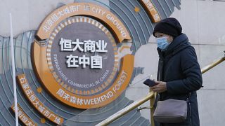 A woman passes by a display showing Evergrande's China commercial projects in Beijing, China, Tuesday, Dec. 7, 2021.