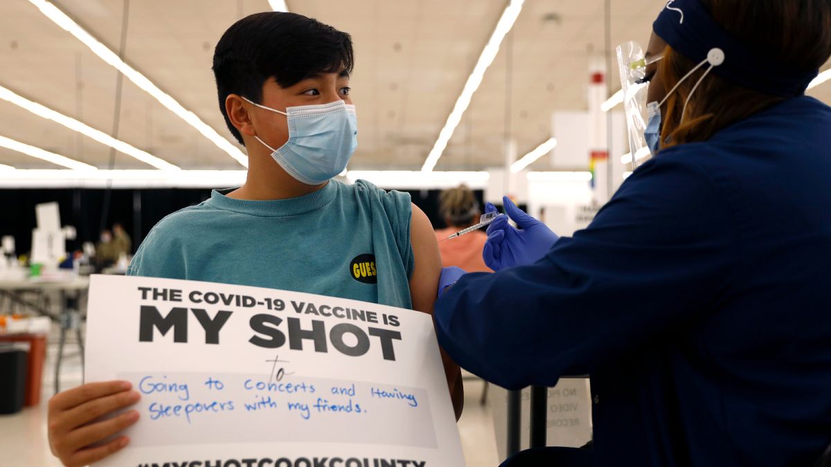 Lucas Kittikamron-Mora, 13, holds a sign in support of COVID-19 vaccinations as he receives his first Pfizer dose at the Cook County Public Health Department, May 13, 2021.
