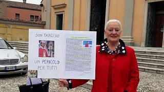 Silvia de Martini stands outside a church in Casorate Primo with a placard denouncing FatherTarcisio Colombo. It reads: "Don Tarcisio, a danger for everyone".