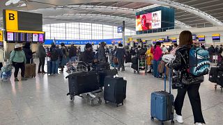 Passengers queue to check in, at Heathrow Airport in London.