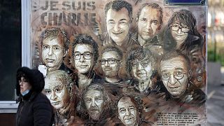 A woman walks past a mural payinng tribute to members of Charlie Hebdo newspaper who were killed by jihadist gunmen in January 2015, on January 6, 2022.