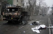 Um cadáver coberto por um cartaz jaz ao lado de um veículo militar incendiado