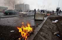 People walk past cars, which were burned after clashes, on a street in Almaty, Kazakhstan, Friday, Jan. 7, 2022.
