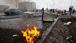 People walk past cars, which were burned after clashes, on a street in Almaty, Kazakhstan, Friday, Jan. 7, 2022.