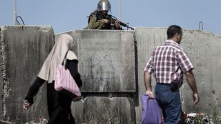 مجندة إسرائيلية تشهر سلاحها عند حاجز قلنديا جنوب رام الله فيما ينتظر آلاف الفلسطينيين للعبور من الضفة الغربية إلى القدس. 2015/07/03