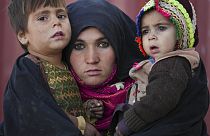 Una mujer afgana sostiene a sus hijos mientras espera una consulta frente a una clínica improvisada en un extenso asentamiento de chozas de adobe que alberga a los desplazados