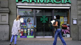 People stop in front of a closed pharmacy in Barcelona.