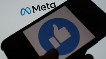 This illustration photo taken in Los Angeles on October 28, 2021, shows a person using Facebook on a smartphone in front of a computer screen showing the META logo