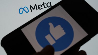 This illustration photo taken in Los Angeles on October 28, 2021, shows a person using Facebook on a smartphone in front of a computer screen showing the META logo