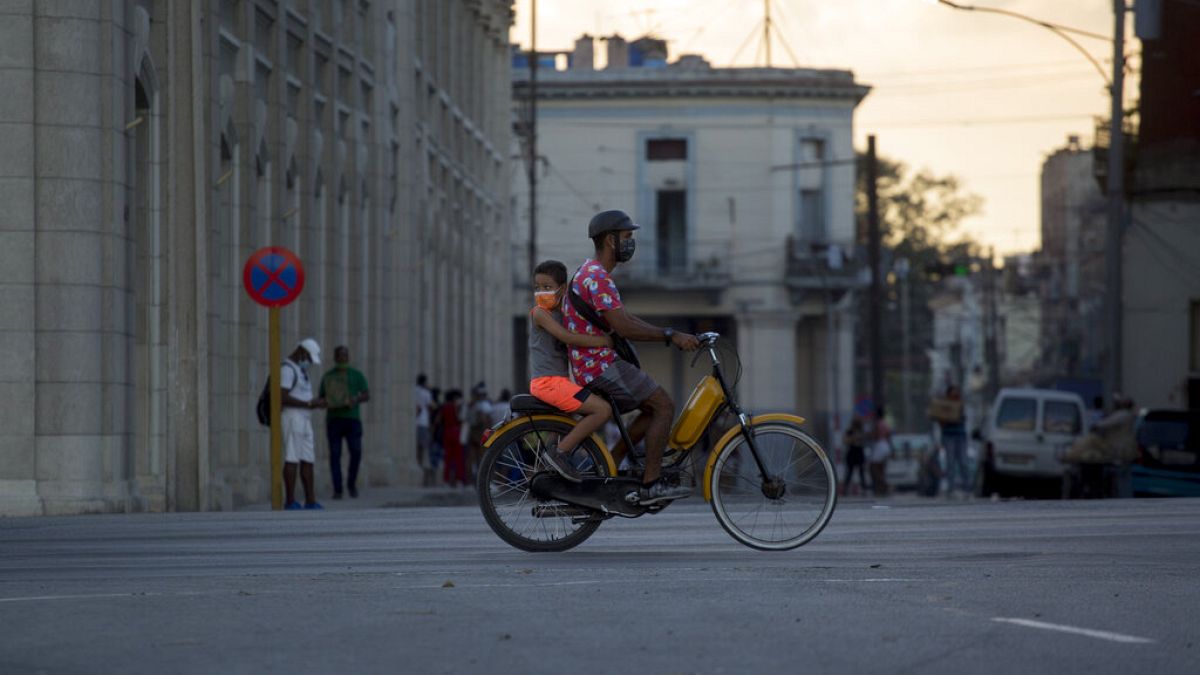 Un uomo e un bambino, indossando maschere protettive, passano in bicicletta all'Avana, Cuba, giovedì 30 dicembre 2021