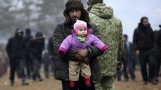 مهاجر يحمل طفلا في مخيم للمهارجين أقيم عند الحدود البولندية مع بيلاروس. نوفمبر 2021