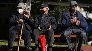 Three elderly men wearing FFP2 face masks to curb the spread of coronavirus, sit on a bench in Athens, Greece, Monday, Jan. 3, 2022