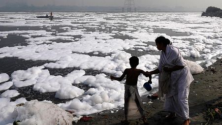 A woman stops her son going in the Yamuna River, covered by a chemical foam caused by industrial and domestic pollution, for bathing, in New Delhi.
