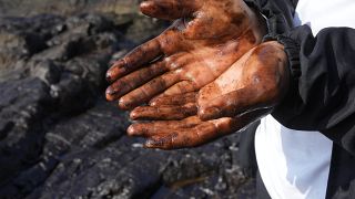 Olajjal szennyezett kezét mutatja egy kerékpáros a perui Ventanilla Cavero tengerpartján 2022. január 18-án,