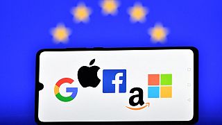 Google, Apple, Facebook, Amazon and Microsoft displayed on a mobile phone with an EU flag displayed in the background.