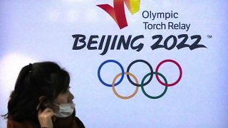 امرأة ترتدي قناعًا للوجه تمر بالقرب من شعار أولمبياد بكين الشتوى 2022