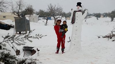 Displaced children standing next to a snowman at a camp for internally displaced people