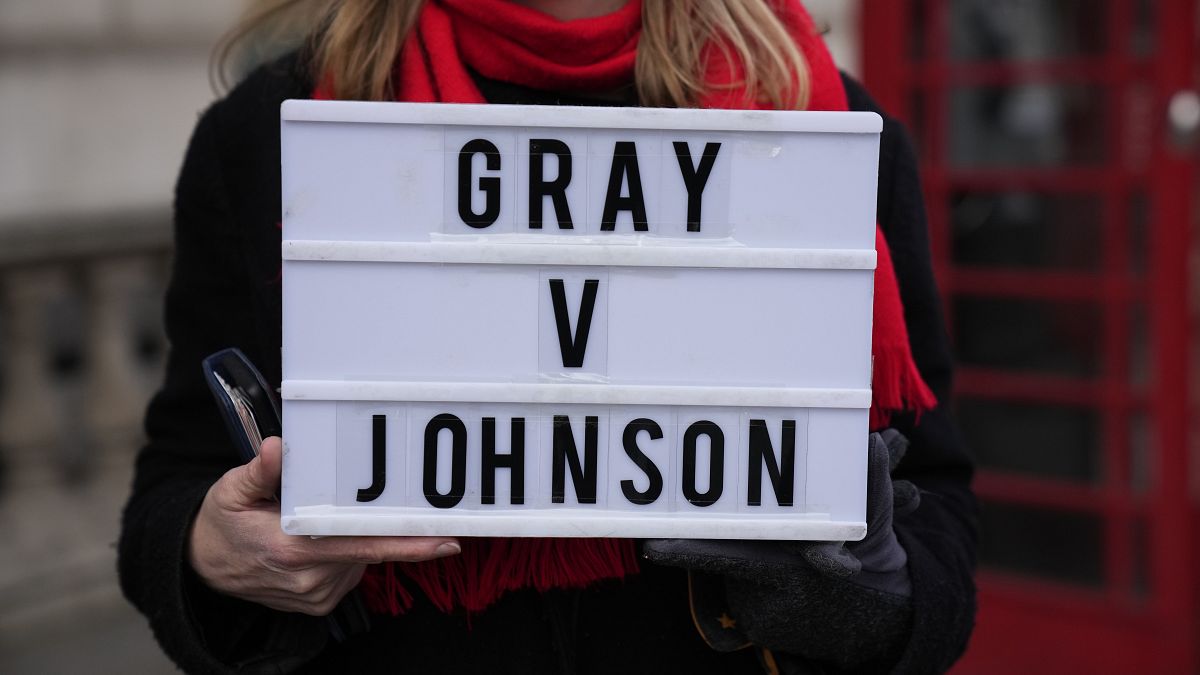An anti-Boris Johnson protester holds a placard as a reference to the Sue Gray report, on the junction of Parliament Street and Parliament Square, in London, Jan. 26, 2022.