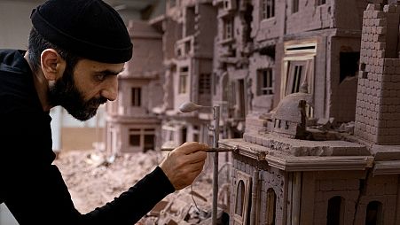 Syrian sculptor Khaled Dawwa works on a clay artpiece, representing a street in Syria destroyed by Syrian regime forces, in his workshop in Vanves, near Paris, January 9, 2022