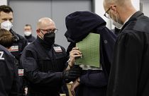 One of the suspected thieves hides his face as he is led into the Higher Regional Court in Dresden.