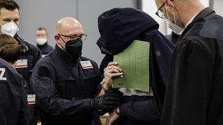 Einer der Angeklagten betritt das Landgericht Dresden in Handschellen und verdeckt sein Gesicht.