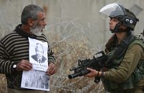 متظاهر فلسطيني يحمل صور الزعيم الجنوب أفريقي الراحل نيلسون مانديلا والزعيم الفلسطيني الراحل ياسر عرفات أمام جندي إسرائيلي. 2013/12/06