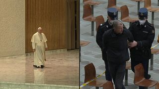 The shouting man is led out of the hall by two Vatican police officers and a Swiss Guard without resisting