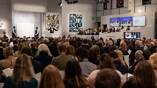 Auctioneer Oliver Barker leads an auction of The Macklowe Collection, alongside Andy Warhol's "Sixteen Jackies" (C) at Sotheby's on November 15, 2021 in New York.