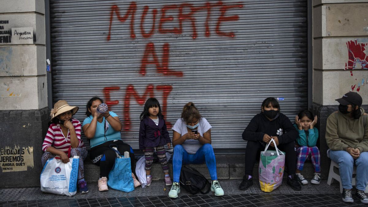 Des manifestants assis devant un graffiti où l'on peut lire en espagnol "Mort au FMI" après une manifestation à Buenos Aires (Argentine), mardi 8 février 2022. 