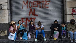 Des manifestants assis devant un graffiti où l'on peut lire en espagnol "Mort au FMI" après une manifestation à Buenos Aires (Argentine), mardi 8 février 2022.