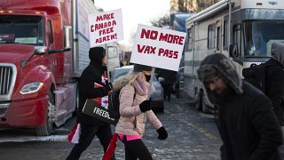 People walk in front of trucks parked on Wellington Street as they join a rally against COVID-19 restrictions on Parliament Hill