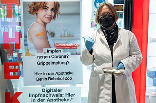 A pharmacist stands outside the pharmacy with vaccination paraphernalia, next to a poster advertising the Corona vaccination in Berlin, Germany, Feb. 7, 2022.