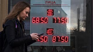 A woman walks past an currency exchange office screen displaying the exchange rates of U.S. Dollar and Euro to Russian Rubles, in Moscow.