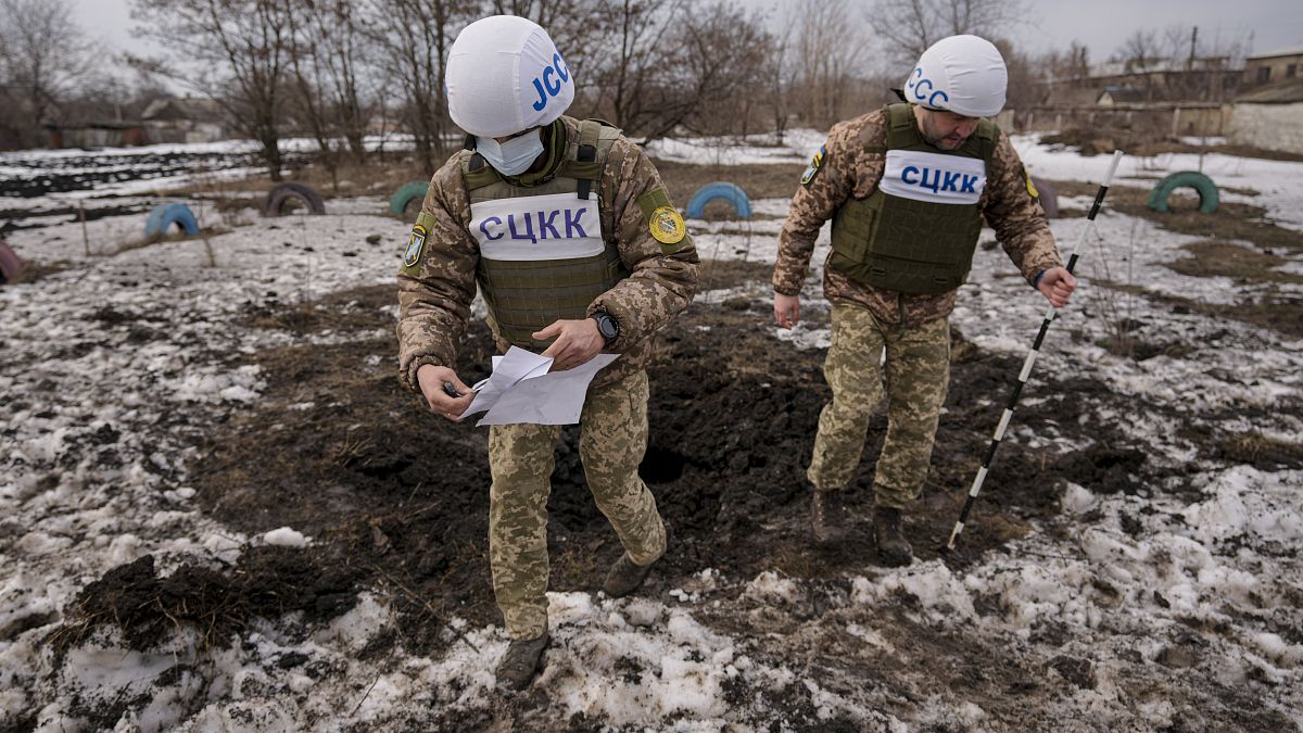 Az orosz-ukrán egyesített ellenőrző és koordináló központ (JCCC) tagjai egy tüzérségi lövedék által okozott krátert vizsgálnak a kelet-ukrajnai Luhanszk megyében 