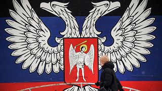 Une habitante de Donetsk passant devant un mur de la ville recouvert de l'emblème de la République populaire de Donetsk, le 19 janvier 2022