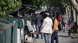 People look at books and posters as they walk past booksellers "bouquinistes", near the river Seine