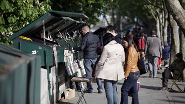 People look at books and posters as they walk past booksellers "bouquinistes", near the river Seine