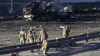 Ukrainian soldiers walk past debris of a burning military truck on a street in Kyiv, Ukraine, Saturday, Feb. 26, 2022. Russian troops stormed toward Ukraine's capital Saturday