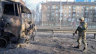 Ukrán katona egy kiégett katonai teherautó előtt Kijevben 2022.02.26-án