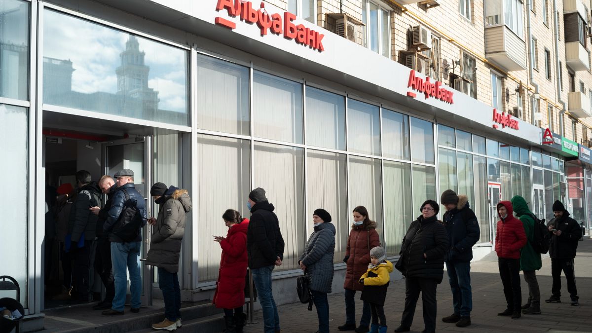 أشخاص يقفون في طابور لسحب الأموال من ماكينة الصراف الآلي التابعة لبنك ألفا في موسكو - روسيا.