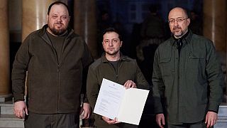 Volodimir Zelenszkij ukrán elnök (középen) Ruszlan Sztefancsuk házelnök és Denisz Smihal kormányfő jelenlétében mutatja Ukrajna EU-csatlakozási kérelmét az aláírás után.