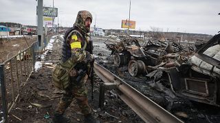 An armed man stands by the remains of a Russian military vehicle in Bucha, close to the capital Kyiv, Ukraine, Tuesday, March 1, 2022.