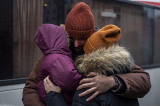 Kyiv resident, holding his daughter and hugging his wife, next to bus destined for Poland at Lviv central station.