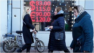 أشخاص يمرون عبر شاشة مكتب صرف تعرض أسعار صرف الدولار واليورو مقابل الروبل في موسكو