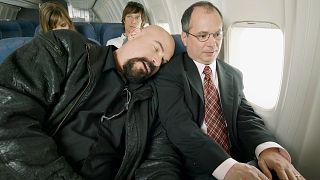 A man falls asleep on a businessman on a plane