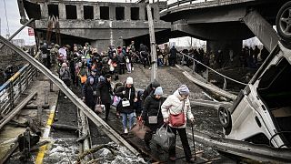 أشخاص يعبرون طريقًا تحت جسر مدمر أثناء فرارهم من مدينة إيربين في أوكرانيا.